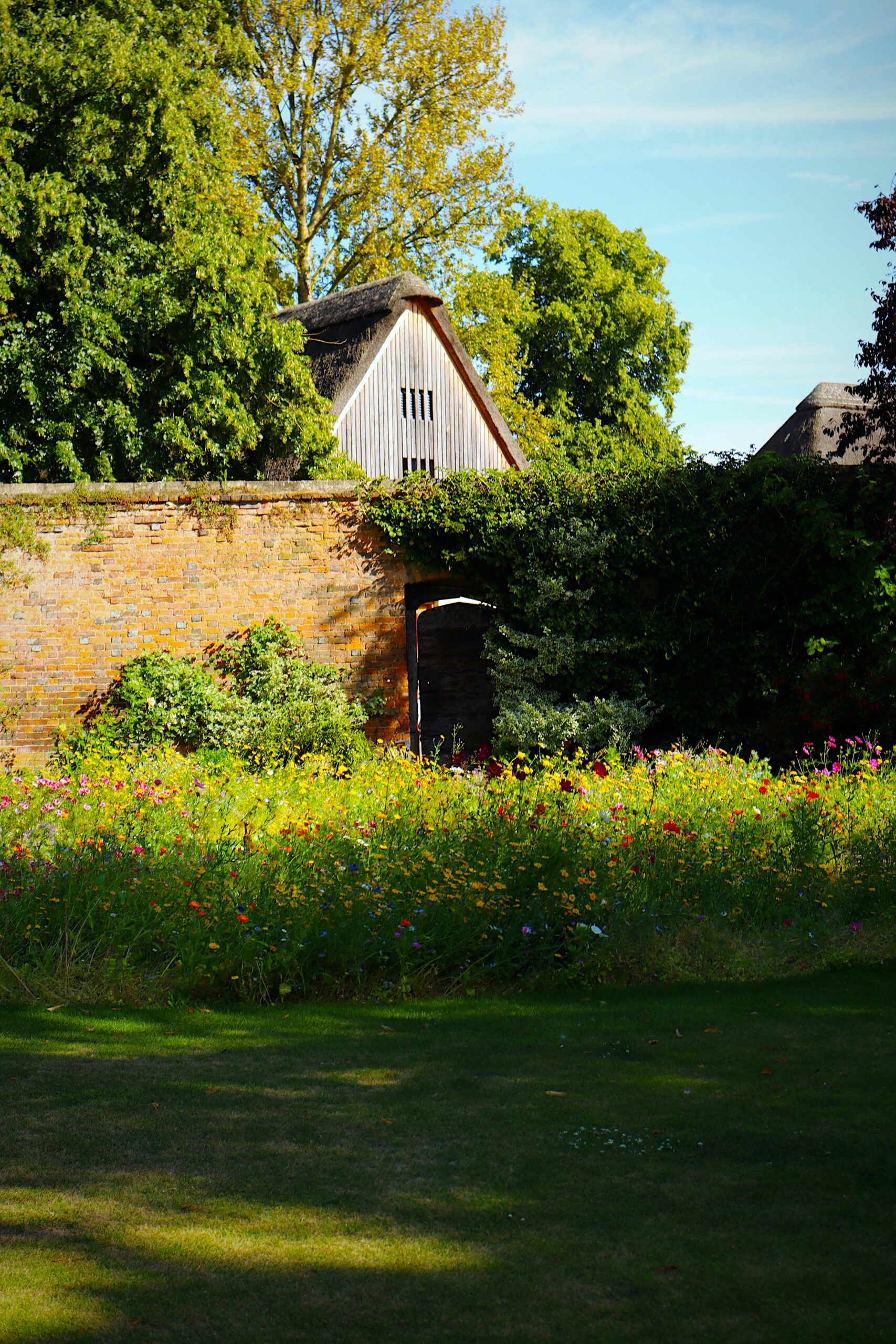 Kolorowy ogród w Oksfordzie z zabytkowym ceglanym murem i rustykalną stodołą.