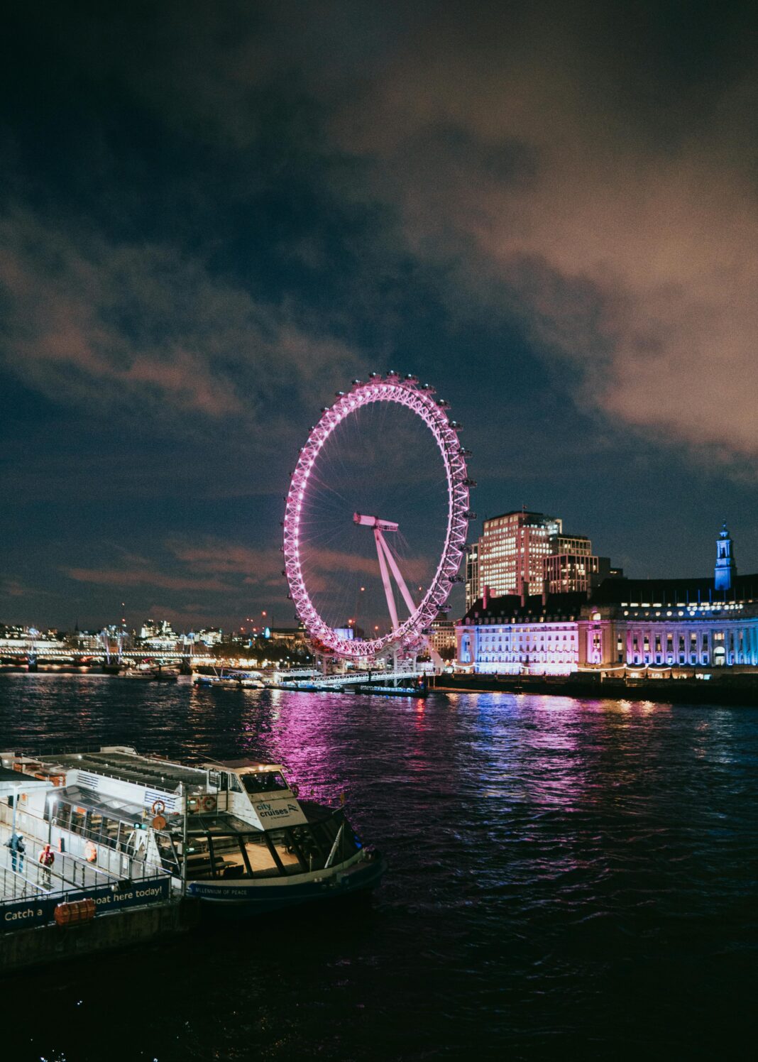 Majestatyczny widok na oświetlone London Eye odbijające się nocą na Tamizie.