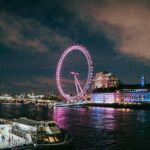Majestatyczny widok na oświetlone London Eye odbijające się nocą na Tamizie.