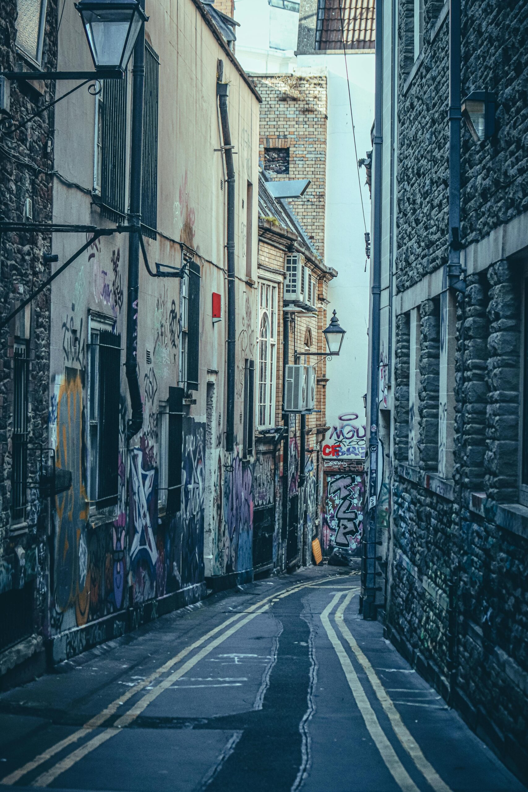 Odkryj pełną graffiti wąską uliczkę w Bristolu, prezentującą architekturę miejską i sztukę uliczną.