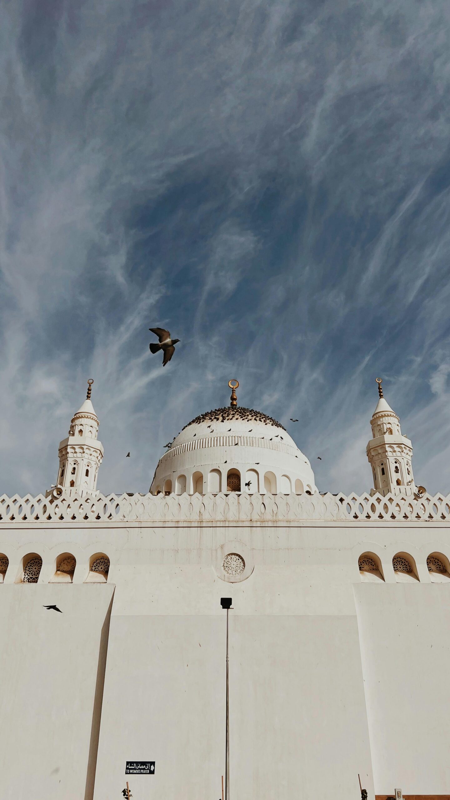 Widok z niskiego kąta na kultowy meczet Masjid Al-Qiblatayn w Medynie, ukazujący jego oszałamiającą architekturę pod dramatycznym niebem.