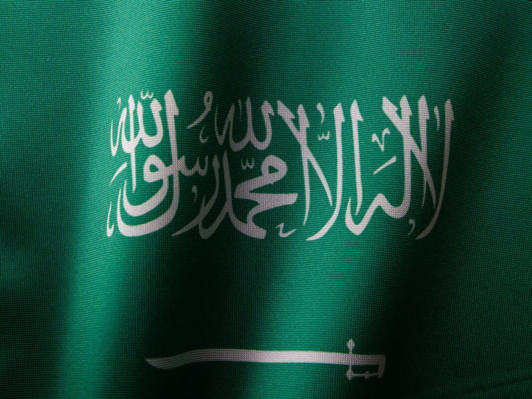 Szczegółowe zbliżenie flagi Arabii Saudyjskiej z eleganckim pismem arabskim i żywym zielonym kolorem.