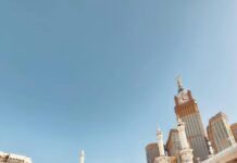 Duży tłum pielgrzymów w Masjid al-Haram w Mekce z widoczną wieżą zegarową Kaaba i Abraj Al Bait.