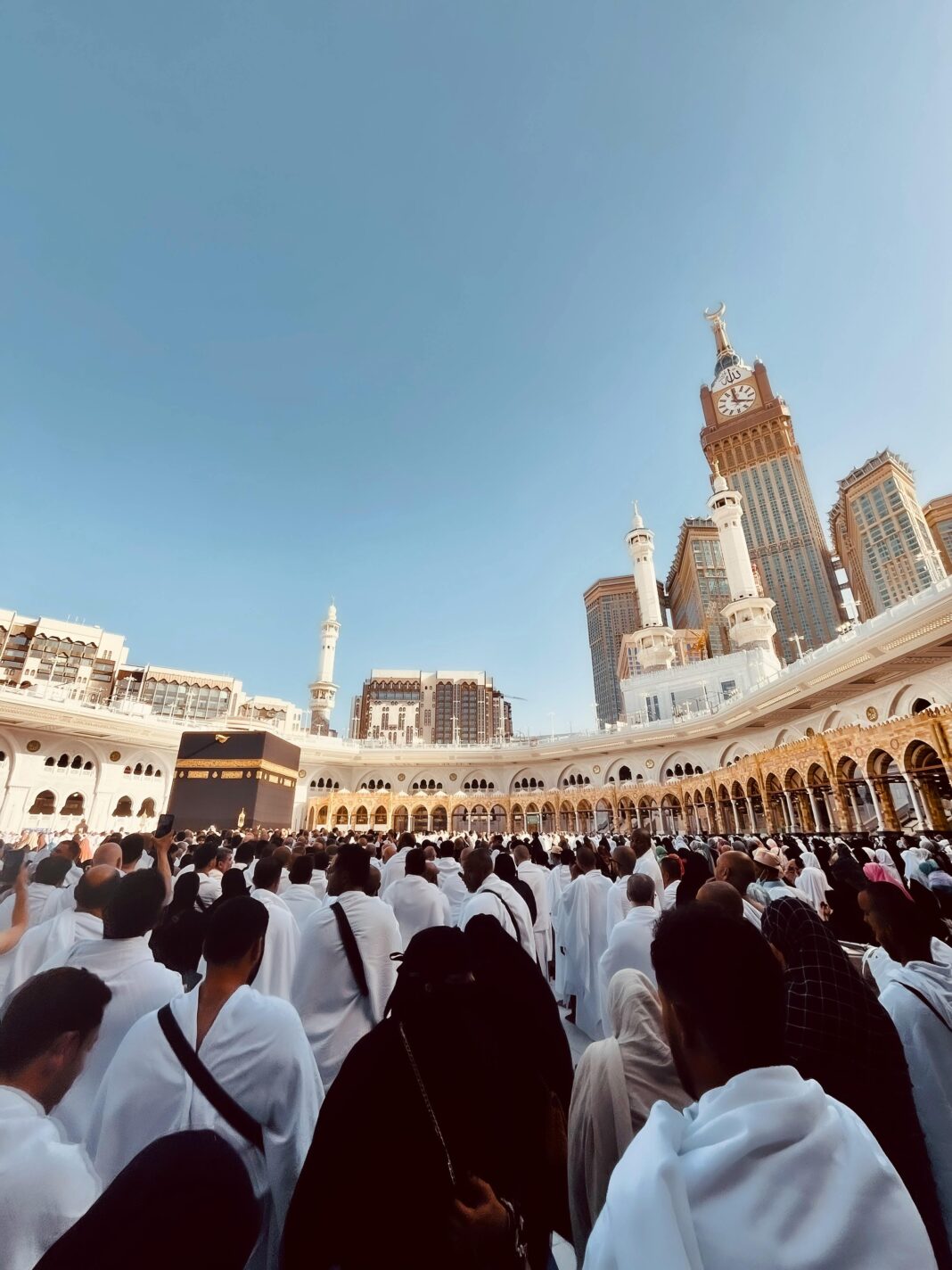 Duży tłum pielgrzymów w Masjid al-Haram w Mekce z widoczną wieżą zegarową Kaaba i Abraj Al Bait.