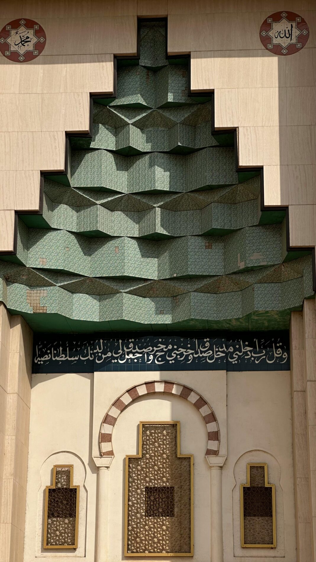 Skomplikowana fasada meczetu z wzorami geometrycznymi i kaligrafią arabską z tradycyjnymi islamskimi elementami.