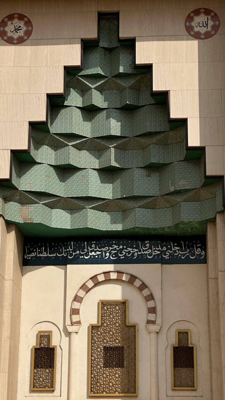 Skomplikowana fasada meczetu z wzorami geometrycznymi i kaligrafią arabską z tradycyjnymi islamskimi elementami.