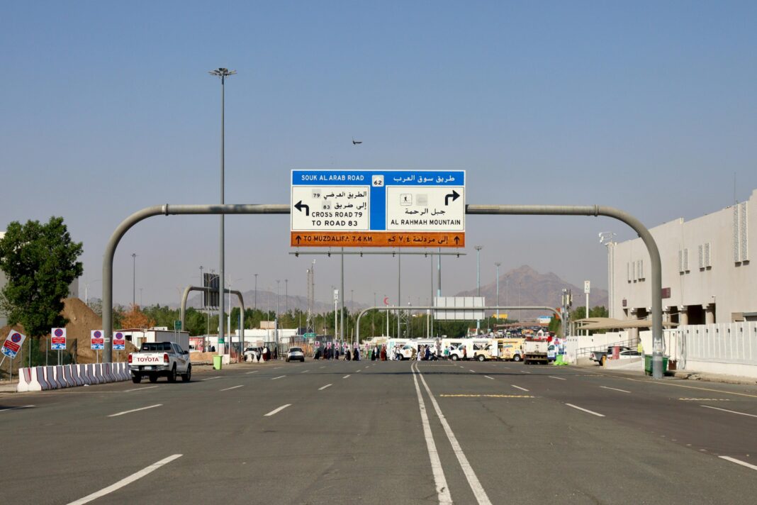 arabia-saudyjska Oznakowanie drogowe prowadzące do góry Al Rahmah w Mekce, z pojazdami i ludźmi w słoneczny dzień.