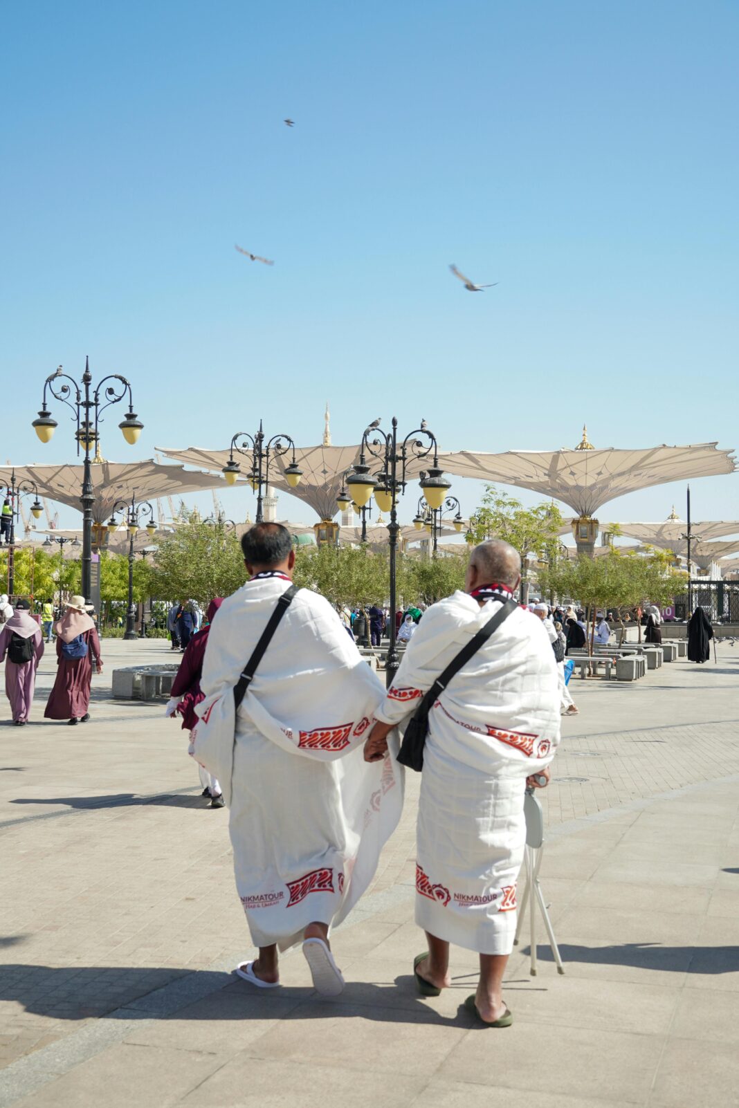 arabia-saudyjska Pielgrzymi w tradycyjnych strojach spacerujący na świeżym powietrzu w Medynie w Arabii Saudyjskiej z parasolami w tle.