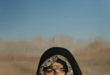 TOP 15 zabytków Arabii Saudyjskiej wartych uwagi Kobieta ubrana w tradycyjny strój beduiński z biżuterią w postaci monet w pustynnym krajobrazie.