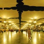 Oświetlona scena nocna na dziedzińcu Masjid Nabawi w Medynie w Arabii Saudyjskiej, przedstawiająca architekturę i parasole.