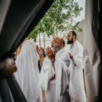 Grupa mężczyzn w białych szatach uczestniczy w duchowej modlitwie na świeżym powietrzu, nawiązując do tradycji kulturowych i religijnych.