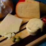 Obserwacja Kondorów w Andach – Skrzydlate Legendy Argentyny Różnorodne sery rzemieślnicze z chlebem i oliwkami na drewnianej desce, idealne do degustacji dla smakoszy.