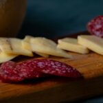 Zbliżenie na plasterki sera i salami na drewnianym talerzu, idealne na przekąski.