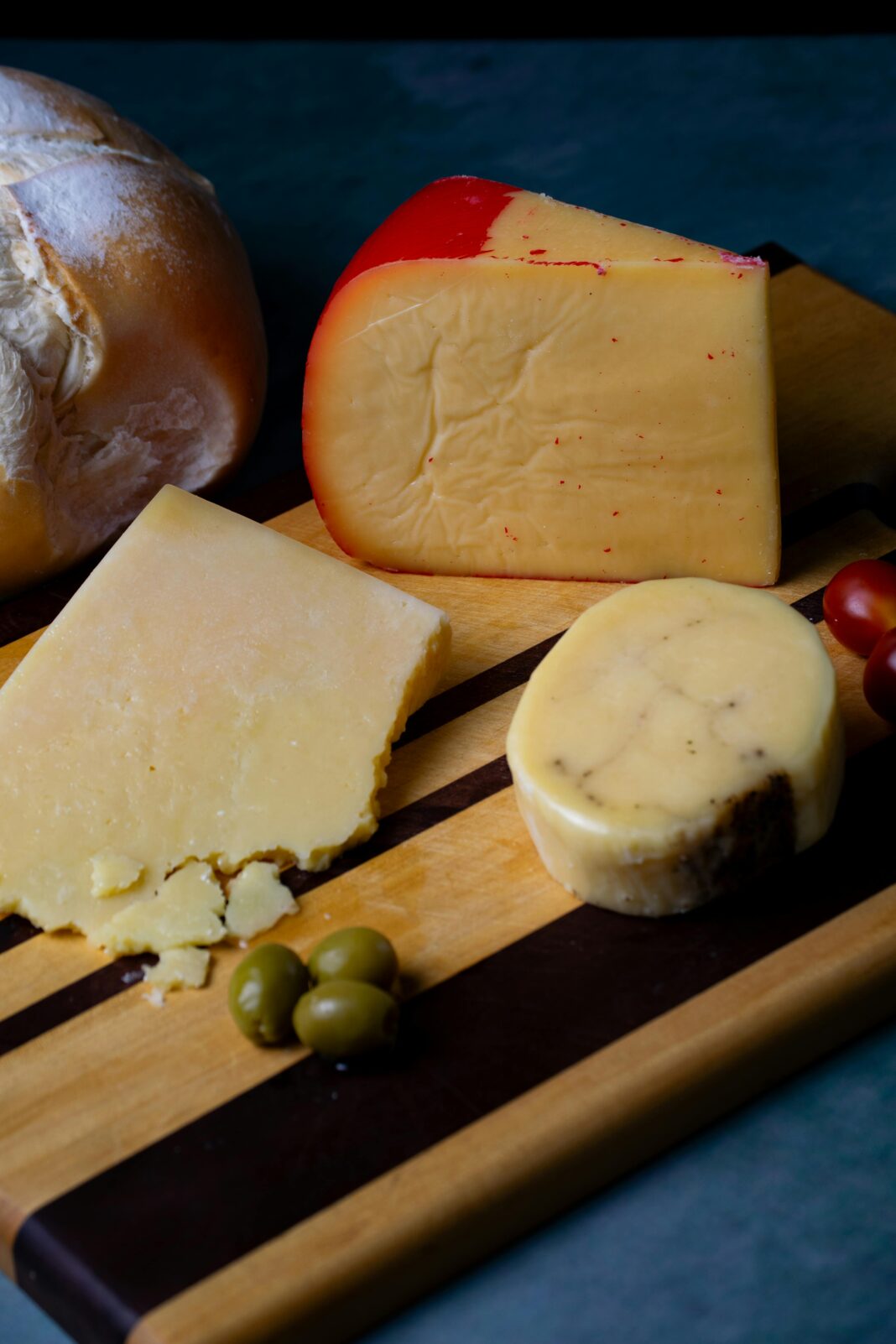 Różnorodne sery rzemieślnicze z chlebem i oliwkami na drewnianej desce, idealne do degustacji dla smakoszy.