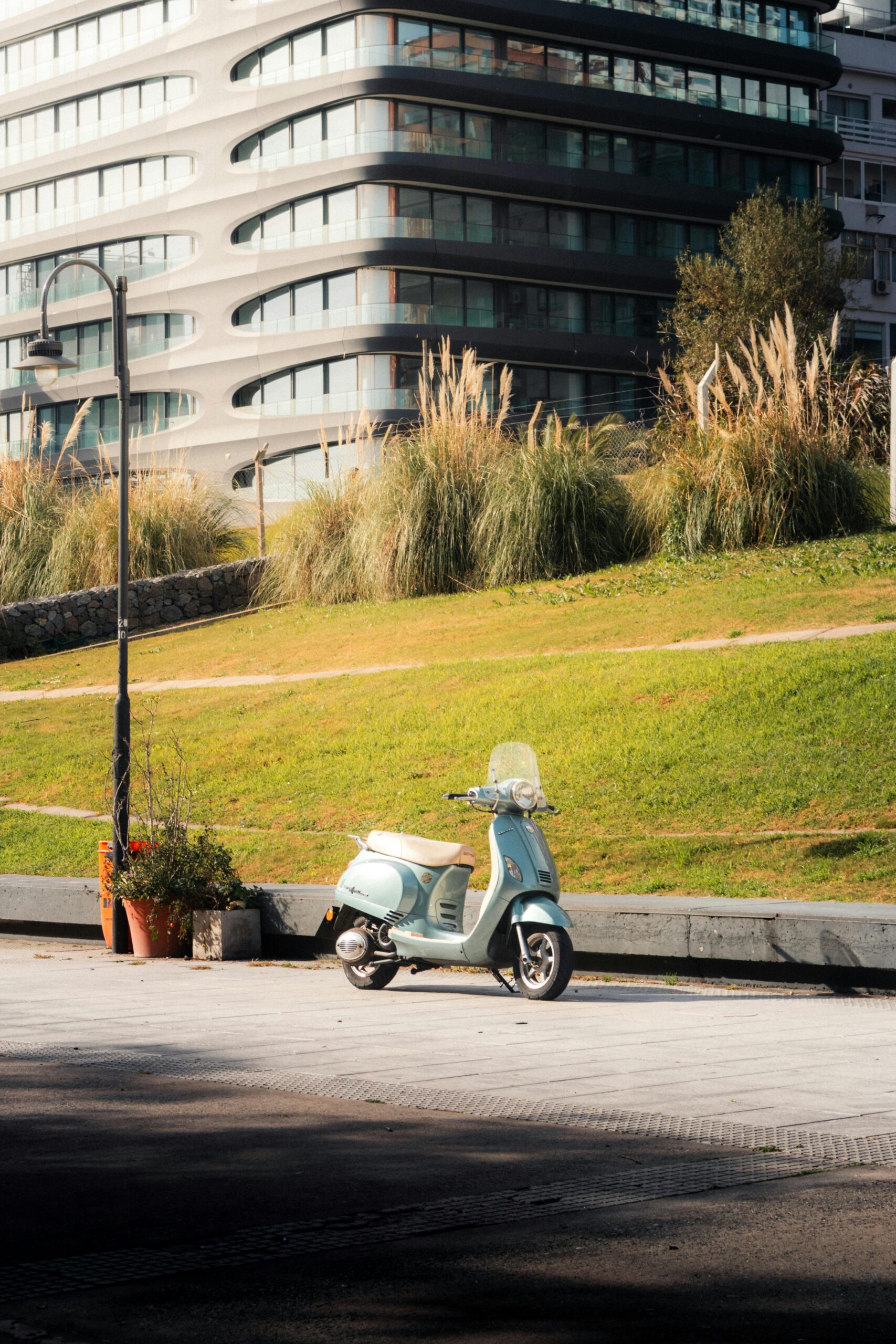 Zabytkowa hulajnoga Vespa zaparkowana w spokojnym parku w Buenos Aires z nowoczesną architekturą w tle.
