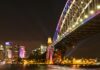 Oszałamiający nocny widok na most Sydney Harbour Bridge z oświetloną panoramą miasta odbijającą się w wodzie.