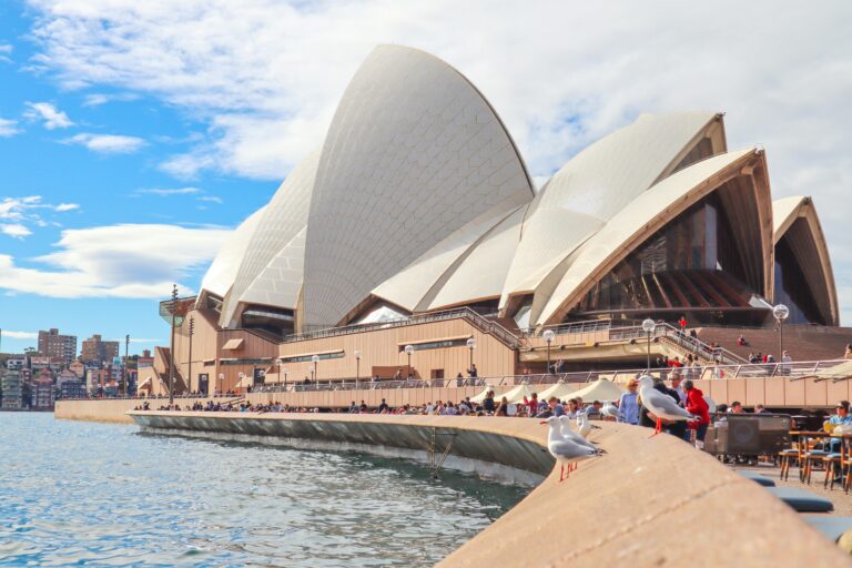 Opera w Sydney z turystami i widokiem na nabrzeże w słoneczny dzień.