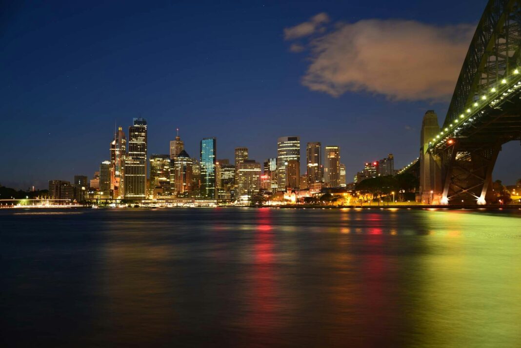 australia Urzekający nocny pejzaż Sydney z oświetloną panoramą i kultowym mostem Harbour Bridge.