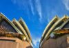 Uderzający widok z niskiego kąta na kultową Operę w Sydney na tle tętniącego życiem błękitnego nieba, ukazujący jej nowoczesny projekt architektoniczny.
