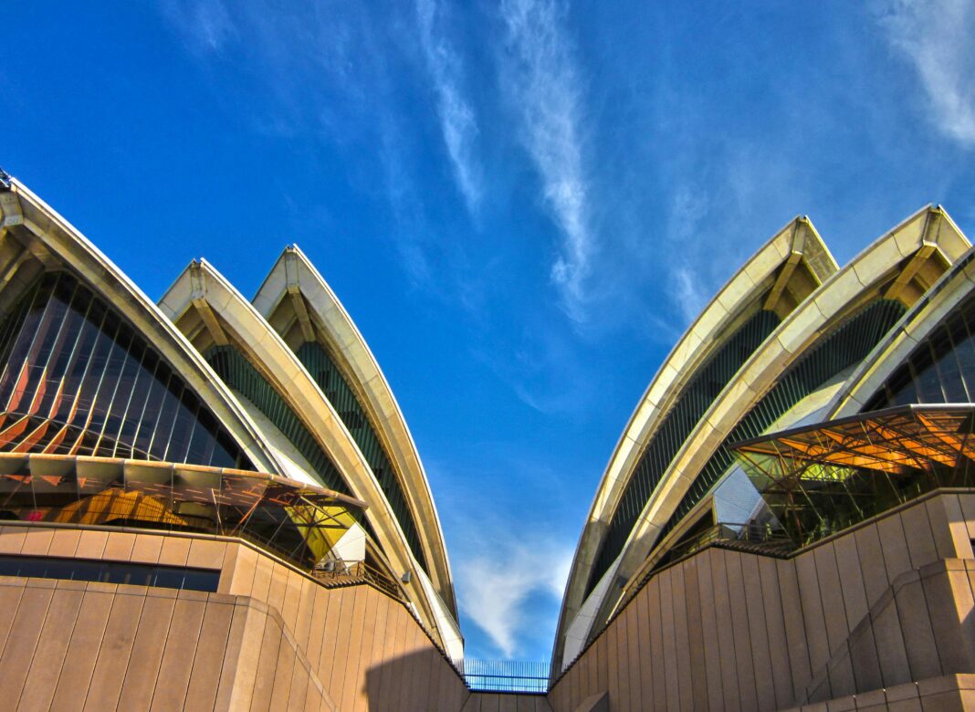 australia Uderzający widok z niskiego kąta na kultową Operę w Sydney na tle tętniącego życiem błękitnego nieba, ukazujący jej nowoczesny projekt architektoniczny.