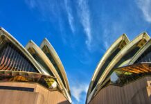Uderzający widok z niskiego kąta na kultową Operę w Sydney na tle tętniącego życiem błękitnego nieba, ukazujący jej nowoczesny projekt architektoniczny.
