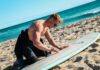 Surfer woskujący deskę na plaży Trigg w Australii, cieszący się słonecznym dniem nad morzem.