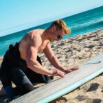 Surfer woskujący deskę na plaży Trigg w Australii, cieszący się słonecznym dniem nad morzem.