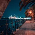 Spokojny nocny widok na Operę w Sydney z chodnika na nabrzeżu, pięknie oświetlony.