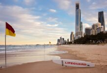 Najlepsze miasta studenckie w Australii Ujęcie plaży Surfers Paradise z panoramą o zachodzie słońca, widoczną tablicą ratownika i flagami.