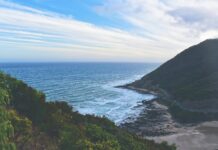 Cairns – baza wypadowa na Wielką Rafę Koralową Hipnotyzujący widok na fale oceanu uderzające w wybrzeże na malowniczym tle wzgórz i nieba.