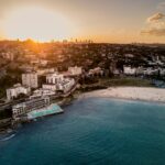 Dlaczego w Australii Boże Narodzenie obchodzi się na plaży? Oszałamiający widok z lotu ptaka na plażę Bondi w Sydney o zachodzie słońca, ukazujący wybrzeże i krajobraz miasta.
