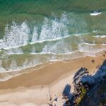 Zapierające dech w piersiach zdjęcie lotnicze przedstawiające fale rozbijające się o dziewiczą piaszczystą plażę.