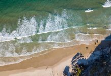 Zapierające dech w piersiach zdjęcie lotnicze przedstawiające fale rozbijające się o dziewiczą piaszczystą plażę.