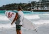 Mężczyzna trzymający deskę surfingową na plaży Bondi w Sydney, gotowy do surfowania po tętniących życiem falach.