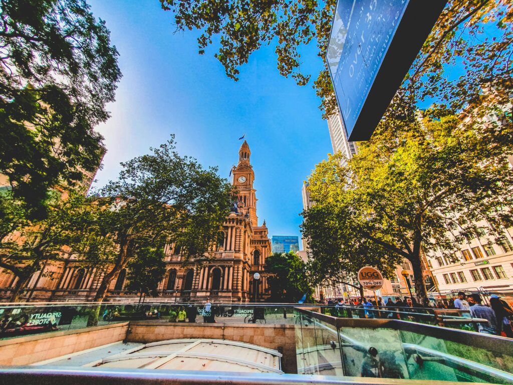Żywy widok na kultową wieżę zegarową w Sydney otoczoną bujną zielenią i miejską architekturą.