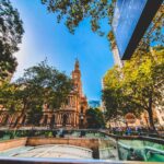 Największe religie w Australii Żywy widok na kultową wieżę zegarową w Sydney otoczoną bujną zielenią i miejską architekturą.