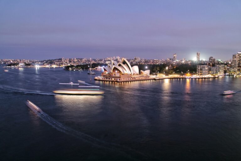 Oszałamiający widok na Operę w Sydney i port oświetlony o zmierzchu, ukazujący życie i architekturę miasta.