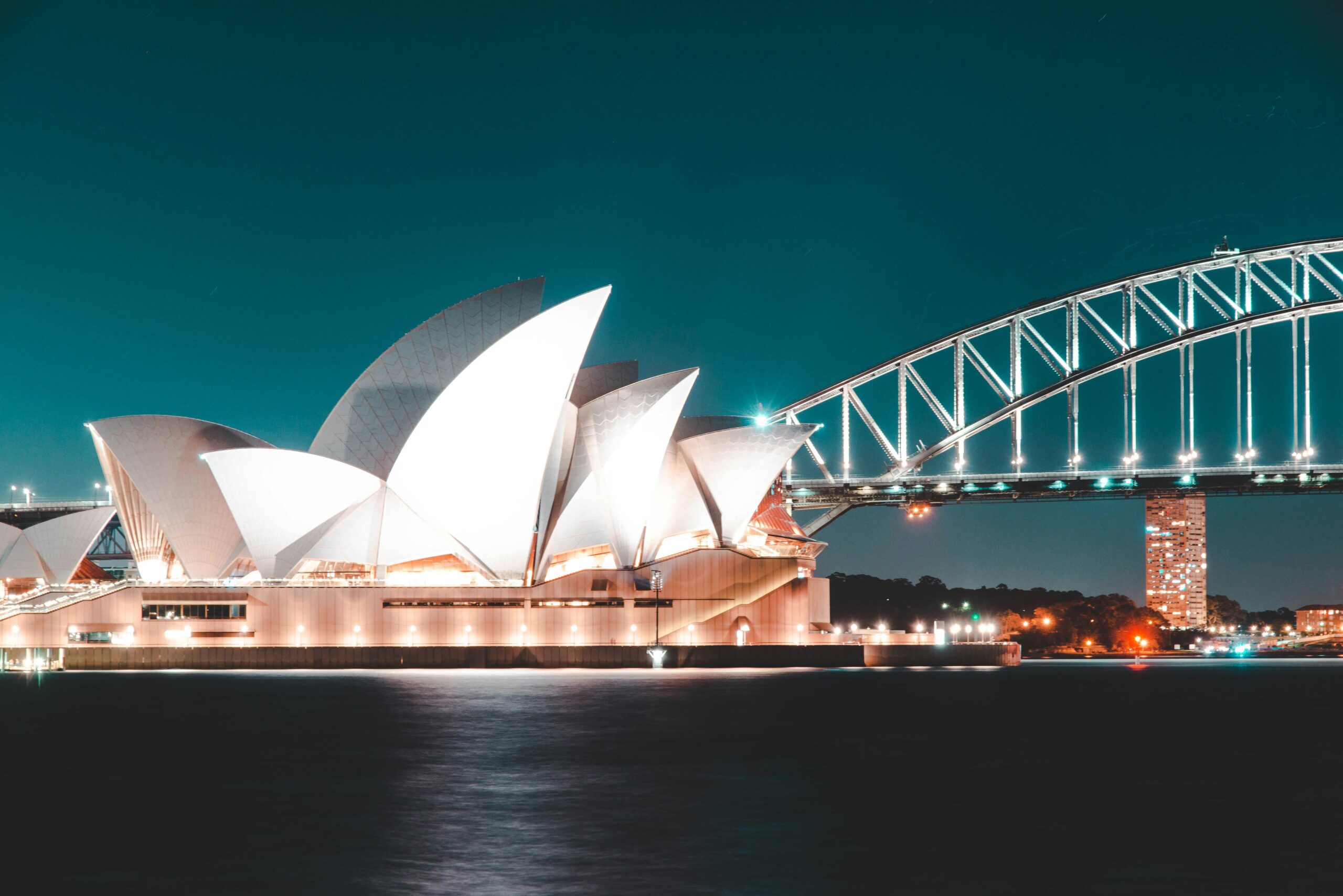 Oszałamiający nocny widok na Operę w Sydney i most Harbour Bridge, pięknie oświetlony na tle czystego nieba.