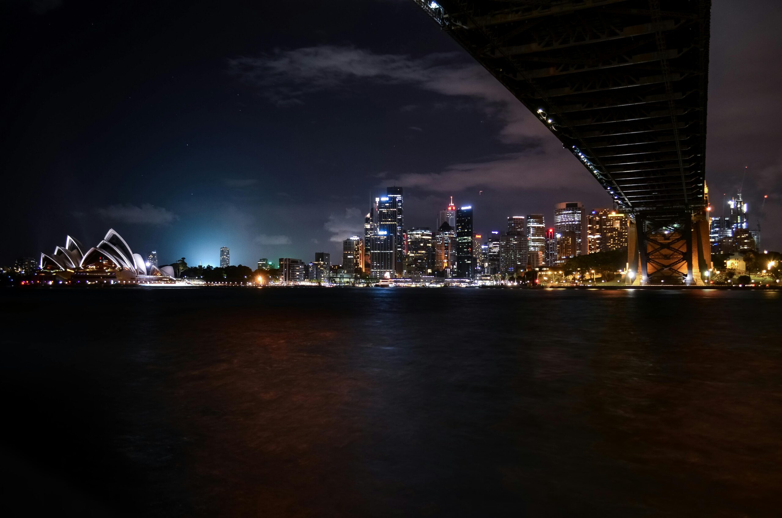 Malowniczy nocny widok na operę w Sydney i panoramę miasta pod mostem Harbour Bridge.