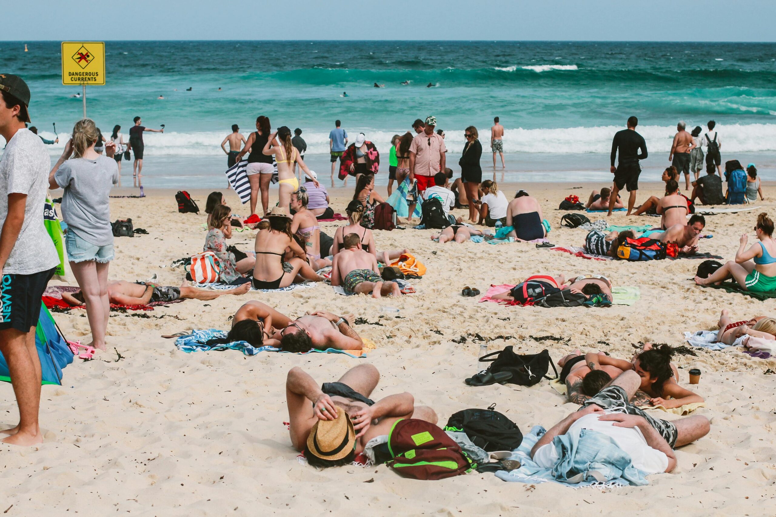 Ludzie cieszący się słonecznym dniem na plaży Bondi w Australii, z żywymi falami oceanu i żywą atmosferą.