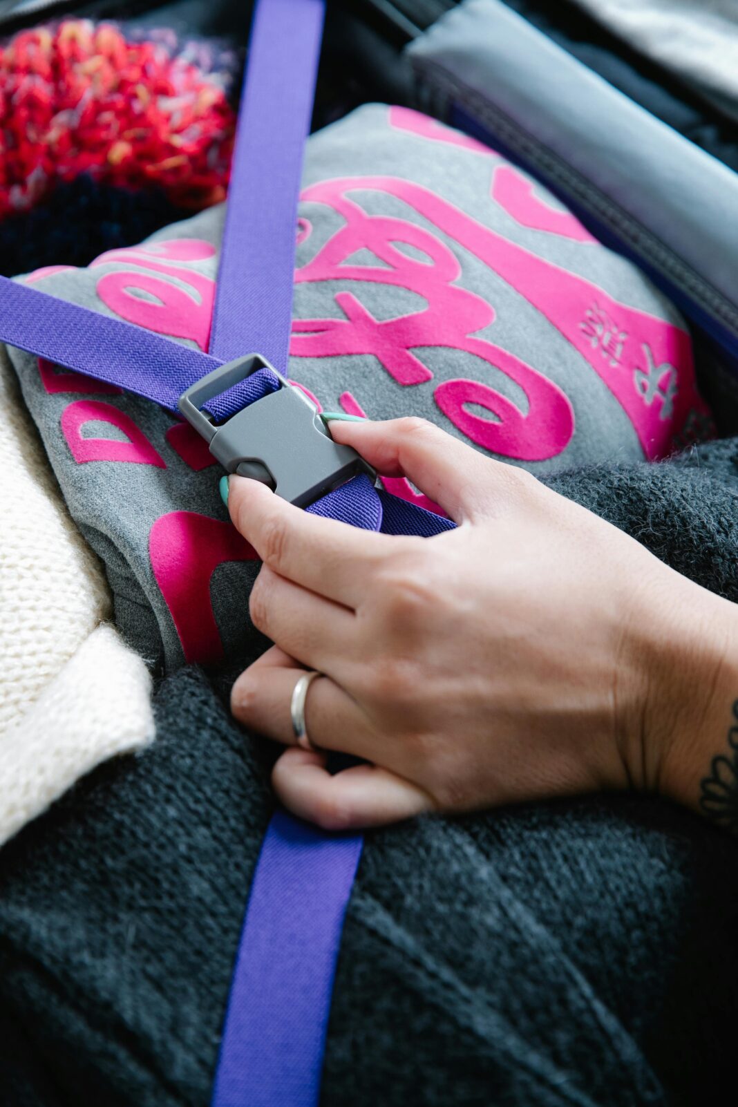 bagaz-podreczny Zbliżenie dłoni zapinającej niebieski pasek na złożone ubrania w walizce, zapewniającej bezpieczne pakowanie.