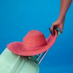 Bagaż podręczny w pociągu vs samolot – co warto wiedzieć? Jasny letni klimat z żywym słomkowym kapeluszem na miętowej walizce, gotowy do podróży.