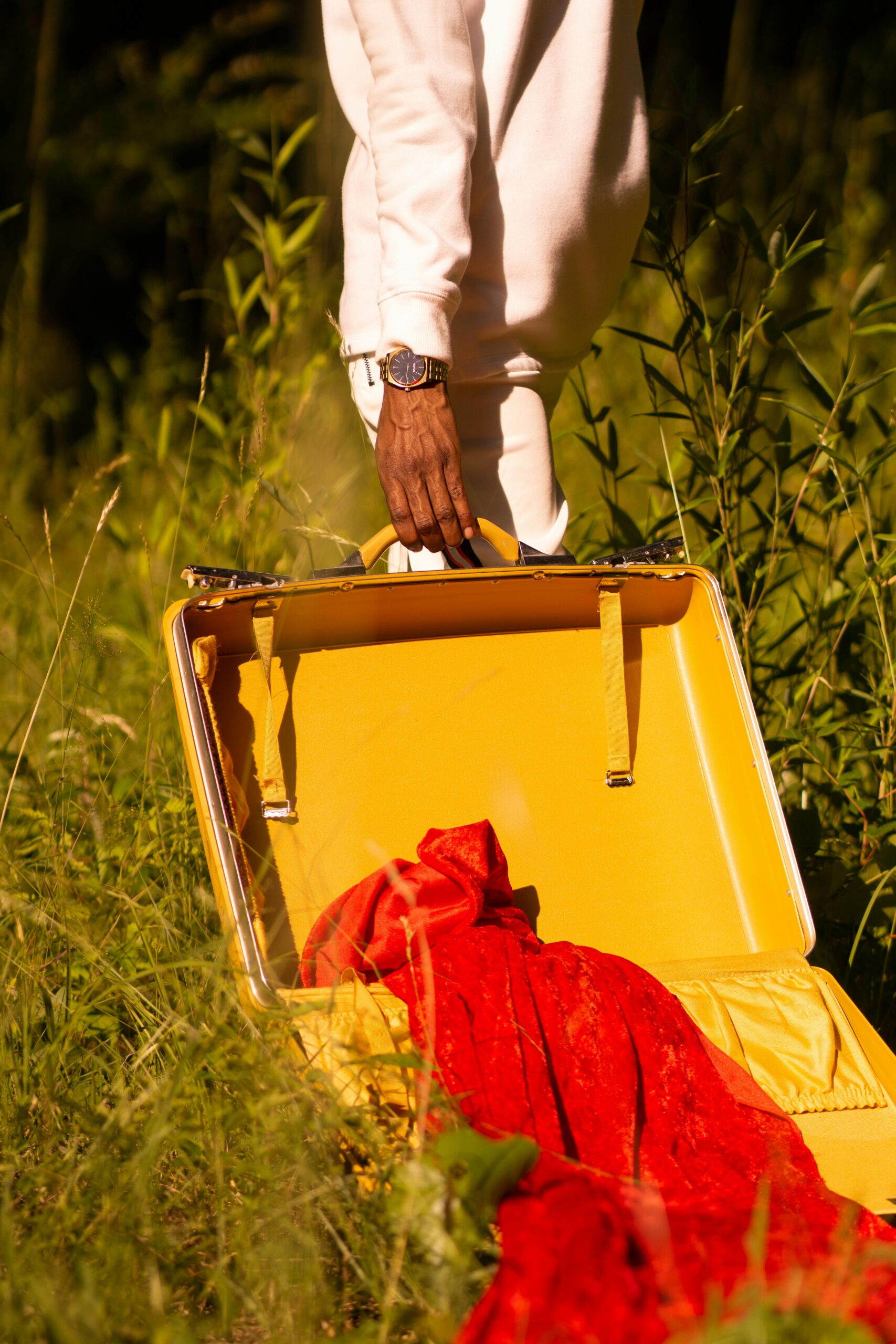 Osoba stojąca z otwartą żółtą walizką na trawiastym terenie na zewnątrz, zawierająca czerwony materiał.