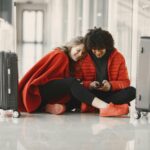 Szczęśliwa para siedzi na podłodze lotniska z bagażem i dzieli się chwilą za pomocą smartfona.