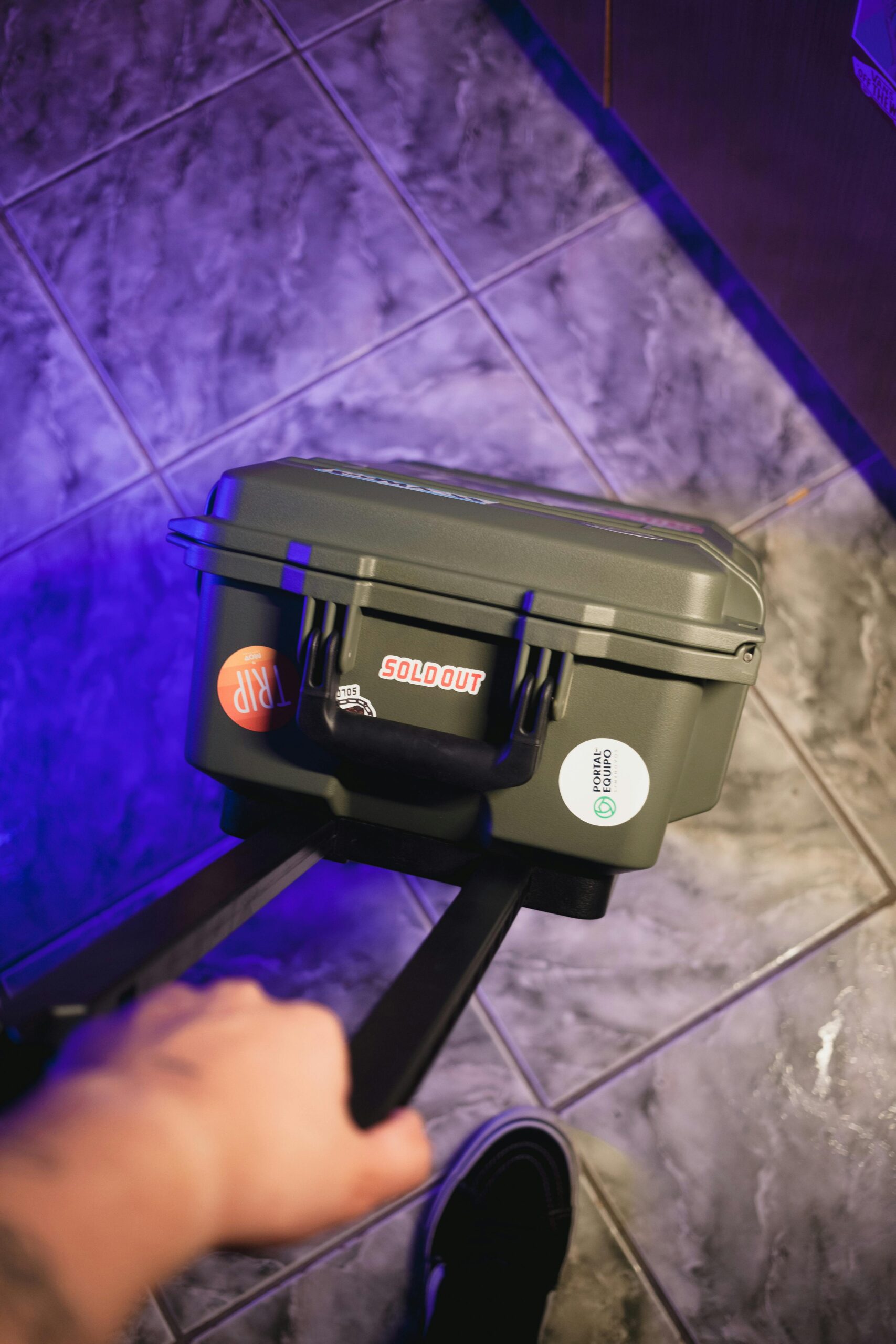 Zbliżenie osoby trzymającej naklejoną walizkę na podłodze wyłożonej kafelkami.