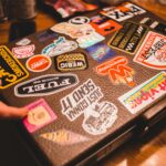 Jakie kosmetyki można wziąć do bagażu podręcznego? Walizka pokryta różnymi kolorowymi naklejkami na drewnianym stole w pomieszczeniu.