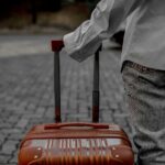 Osoba ciągnąca czerwoną walizkę na brukowanej uliczce, wskazująca podróż lub podróż.