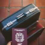 Niezbędne akcesoria podróżne, w tym paszport i walizka na podłodze wyłożonej czerwonymi kafelkami, sugerujące dalszą podróż.