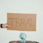 Podręczny ekwipunek na podróże pociągiem – co warto zabrać? Koncepcja kreatywnej podróży obejmująca kartonowy znak, kulę ziemską, paszport i walizkę na białym tle.