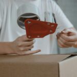 Zbliżenie osoby zaklejającej karton taśmą do pakowania i wysyłki.